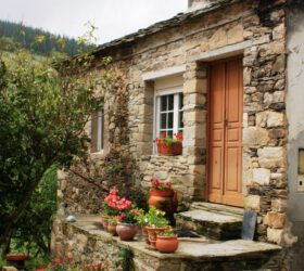 Casa de piedra con arboles y macetas en los peldaños de la entrada
